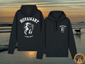 Schwarzer Unisex Hovawart Hoodie mit weißem Siebdruck eines Hovawart-Kopfes und dem Schriftzug "HOVAWART SINCE 1922" auf Rücken und Brusttasche, vor einem Sonnenuntergangshintergrund am Meer