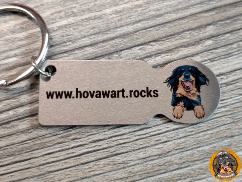 Rückseite eines silberfarbenen Hovawart-Schlüsselanhängers mit der Aufschrift "www.hovawart.rocks" und einer Illustration eines schwarzmarkenen Hovawarts.