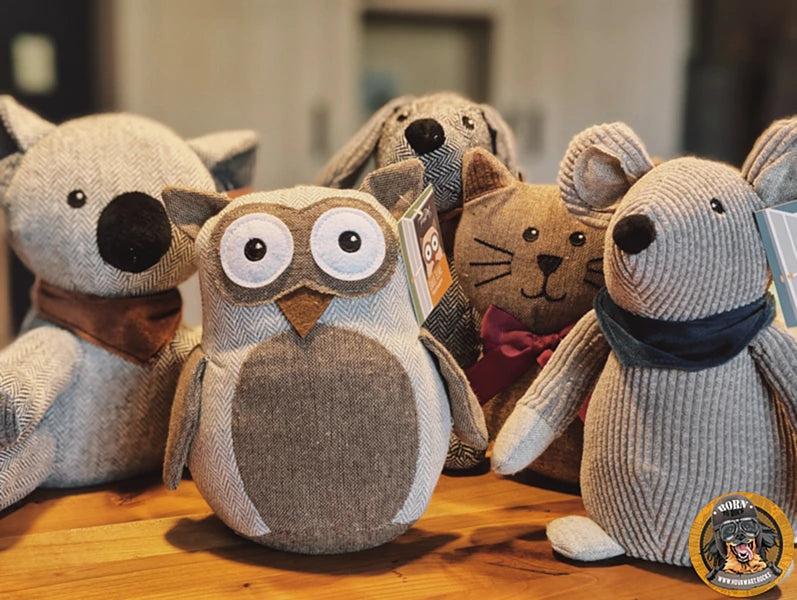 Nahaufnahme von fünf verschiedenen Stoff-Türstoppern in Grautönen und Herringbone-Muster, auf einem Holztisch stehend: Eine Eule (mittig vorn), ein Koala (links), ein Hund (Mitte hinten), eine Katze (rechts hinten) und eine Maus (rechts vorn). Alle Türstopper sind robust und halten Türen offen.