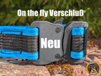 Nahaufnahme eines stabilen, dunkelgrauen Verschlusses an einem blauen und schwarzen Hundehalsband. Der Verschluss ist ein Schnellverschluss mit einem seitlichen Hebel. Auf dem oberen Teil des Bildes steht in weißer Schrift "On the fly Verschluß", und auf dem Verschluss selbst steht in weißer Schrift "Neu". Das Halsband liegt auf einem moosbewachsenen Untergrund. Unten rechts ist das runde Logo "Born to Rock - www.hovawart.rocks" eingeblendet.