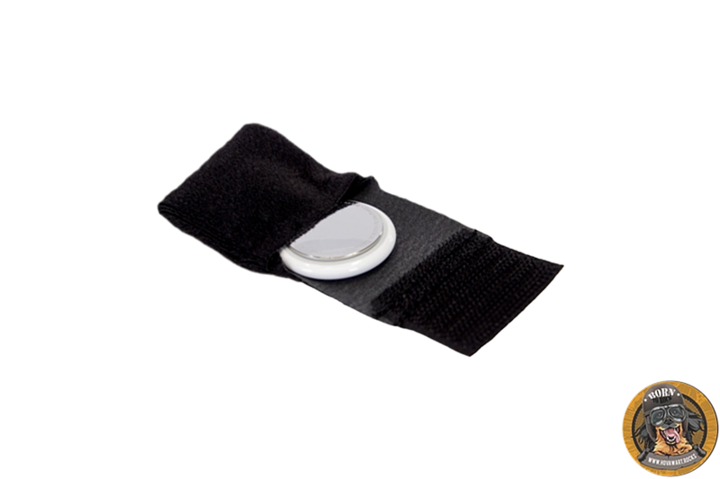 Geöffnete, schwarze AirTag-Tasche mit Klettverschluss. Ein silberner und weißer Apple AirTag liegt in der Mitte der Halterung.